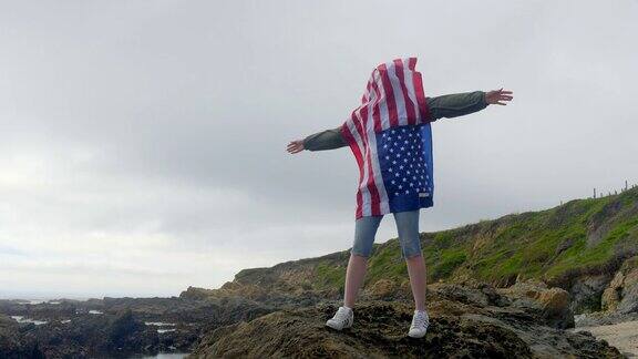 在太平洋狂野海岸的岩石上举着美国国旗的女人加州
