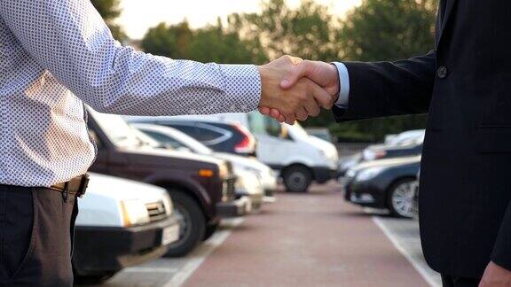 两个不认识的商人互相握手后面停着车经理或客户在室外握手伙伴们在外面握手特写慢动作侧视图
