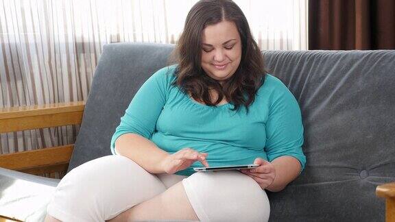 Body-Positive女性胖女孩在沙发上用平板电脑