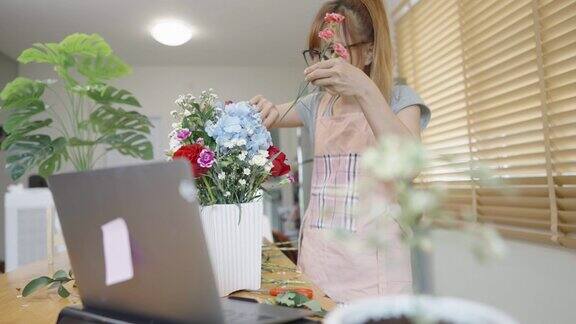 年轻的亚洲女性戴着眼镜在网上教插花并向她的学生挥手