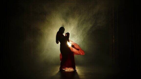 一个穿着红色纱丽的年轻舞女剪影印度的民间舞蹈在有烟雾和霓虹灯的黑暗工作室里拍摄慢动作