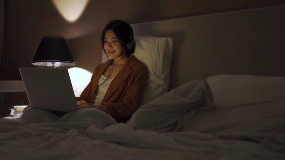 一名年轻的亚洲华人女子晚上在卧室里用笔记本电脑上网