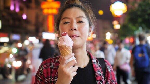 年轻迷人的亚洲女子在晚上的夜市享受华夫蛋筒草莓冰淇淋