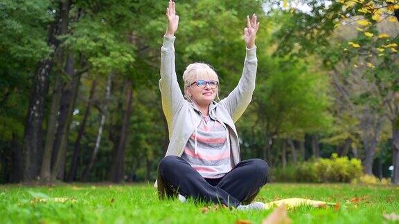 老年退休妇女在公园草坪上的垫子上锻炼老年妇女在大自然中练习莲花姿势