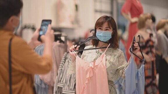 两位亚洲华人女性在服装店戴着口罩挑选衣服
