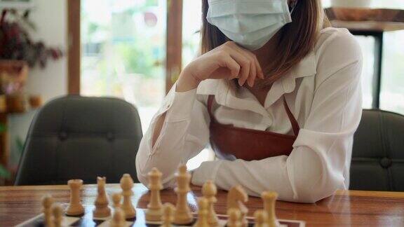 一名年轻的亚洲妇女在下棋时戴着口罩以预防COVID-19