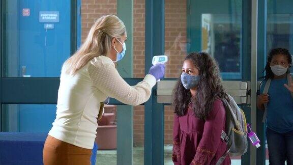 孩子们戴着口罩在学校门口测体温