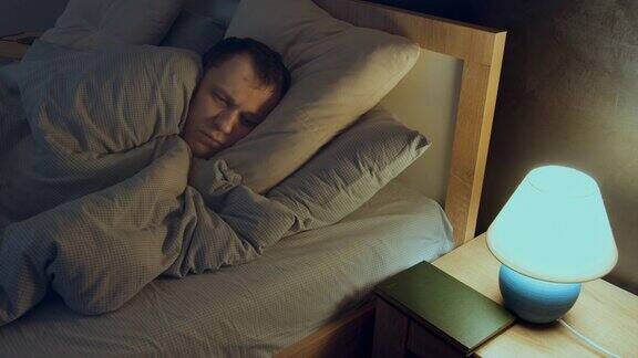 一个男人有失眠症晚上躺在床上睡不着床头桌上的灯就开着