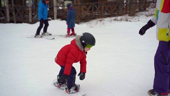 年轻的滑雪板教练教小男孩如何骑滑雪板冬季活动Slowmotion拍摄