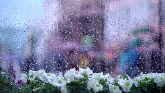 雨天的窗后湿着街头的花和雨点模糊了街头的散景不认识的人拿着雨伞雨天季节现代城市的生活方式