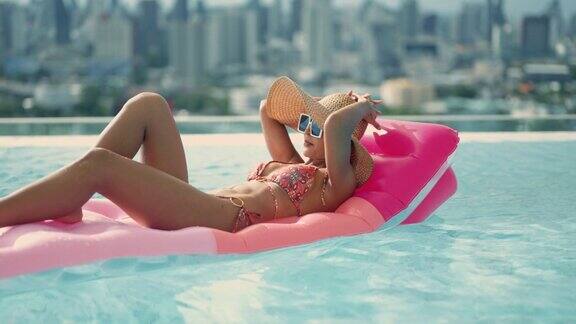 年轻漂亮性感的女孩游泳与粉红色的游泳床垫在游泳池