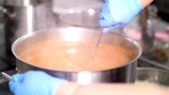 特写镜头厨师戴着防护手套在大平底锅里用大勺子搅拌西红柿汤或罗宋汤健康食品、烹饪、安全理念重新开放食堂