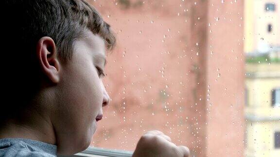 用手指在窗户上玩:孩子在看雨滴落在玻璃上