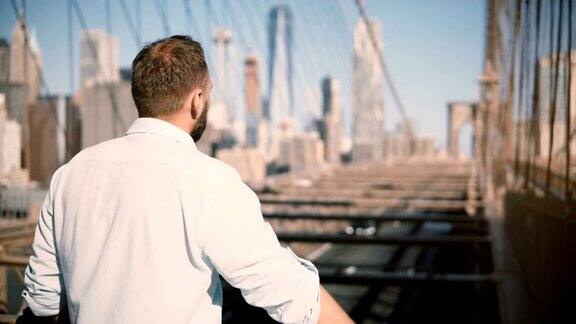 成年白人男子站在布鲁克林大桥栏杆旁欣赏令人惊叹的城市风景并离开4K