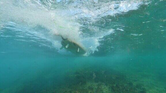 水下慢动作:运动冲浪者划桨在他的冲浪板在清澈的海洋