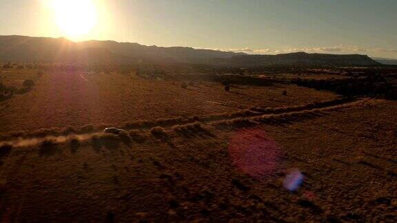 航拍:金色夕阳下一辆黑色SUV行驶在沙漠山谷尘土飞扬的道路上
