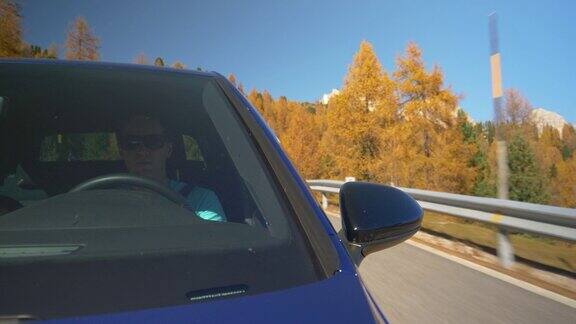 特写:年轻的男游客开着他的蓝色汽车沿着风景优美的山路行驶