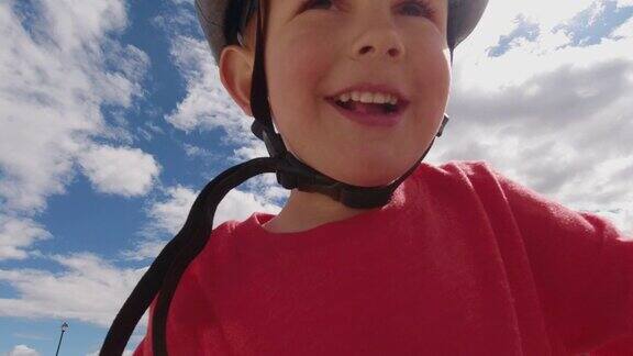 下面是一个四岁的白人男孩戴着自行车头盔微笑着和他三十多岁的白人父亲在多云的天空下骑自行车