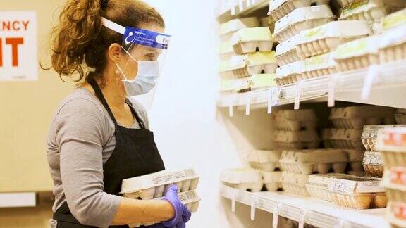 现实生活:超市女员工戴着防护面罩和面罩将冷藏货架装满有机鸡蛋包装