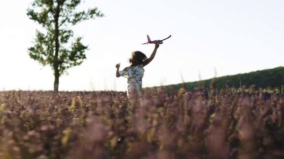女孩拿着飞机在夕阳西下的山坡上奔跑快乐女孩带着玩具飞机在夕阳下的薰衣草田上奔跑孩子们玩玩具飞机概念大孩子梦想