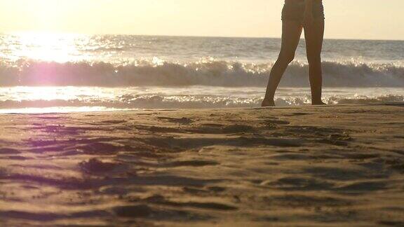 年轻女子的双腿踩在沙子上近距离的女性的脚走在金色的沙滩与海浪的背景光着脚的女孩在海边暑假假期慢动作