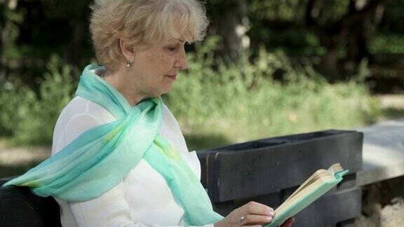 一位年长的女士坐在公园的长椅上看书