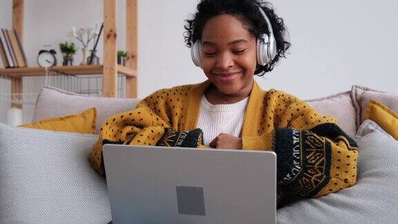 非裔美国女孩使用笔记本电脑在家里视频聊天年轻女子坐在沙发上进行虚拟会议在线聊天视频电话会议在家工作学习远程老师