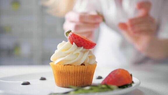 甜点厨师女手装饰美味的纸杯蛋糕白奶油顶部切草莓块在厨房