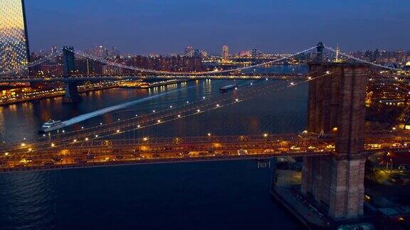从布鲁克林大桥上俯瞰夜晚从曼哈顿驶来的车流背景是曼哈顿中城的在夜晚灯火通明水轮正从桥下驶过无人机视频与平移摄像机运动