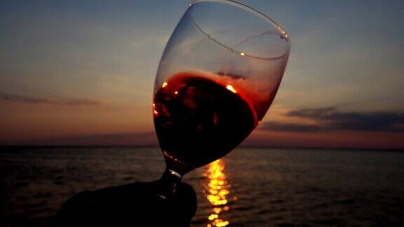 酒杯里的酒映衬着海面上的夕阳缓慢的运动