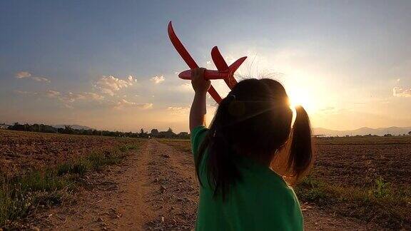 一个快乐的小女孩与一个玩具飞机在一个日落的背景在田野上跑的慢动作幸福家庭理念和童年梦想