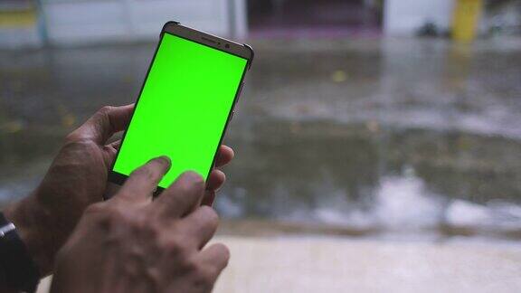 触摸绿色屏幕智能手机与雨背景在城市