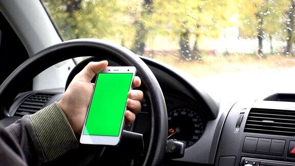一只手拿着一个绿色空白屏幕的智能手机在车里为方向按摩位置业务男人坐在现代汽车里用智能手机工作绿色屏幕特写色度键