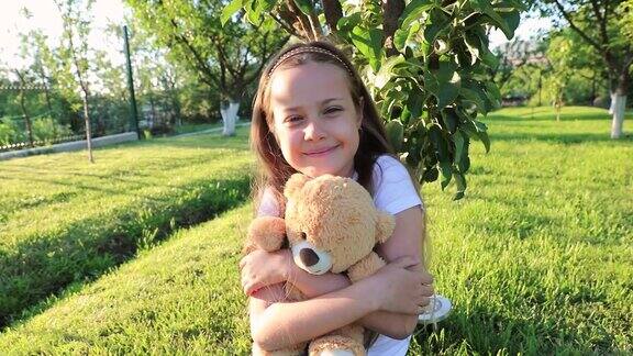 小女孩在绿色的花园里玩一只泰迪熊可爱的小女孩抱着玩具熊