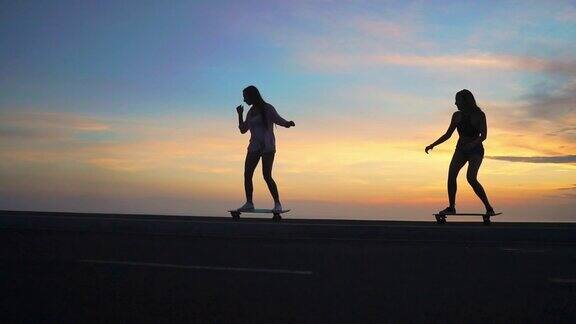 在美丽的初升太阳的映衬下两个穿着短裤和运动鞋的女孩在斜坡上玩滑板慢镜头120帧秒