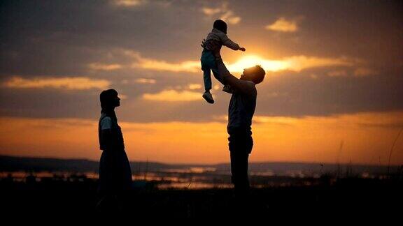 一家人站在夕阳的背景下父亲将儿子抛向空中这是一个夏日的傍晚