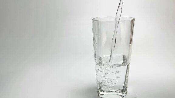 慢镜头从塑料瓶中倒出清水到玻璃杯中背景为白色和灰色