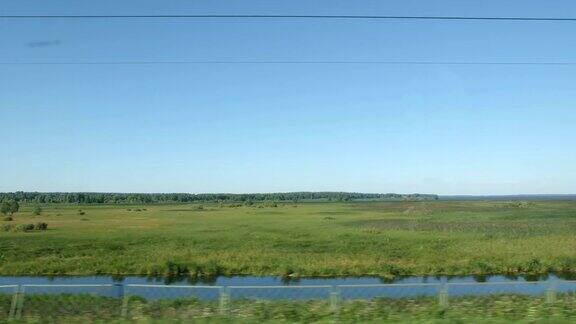 POV:在一个阳光明媚的日子里高速列车驶过一片低矮的森林、绿色的田野和一个湖泊