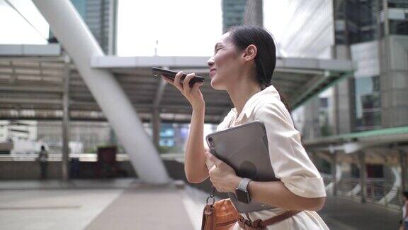 亚洲女人走路用电话语音识别在城市