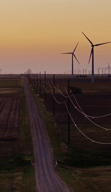 在日出前广阔的堪萨斯风电场涡轮机之间的乡村道路-垂直空中