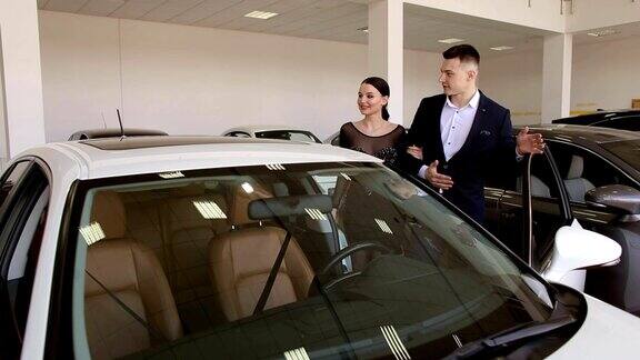 一对年轻夫妇在经销商的展厅里看一辆新的白色汽车