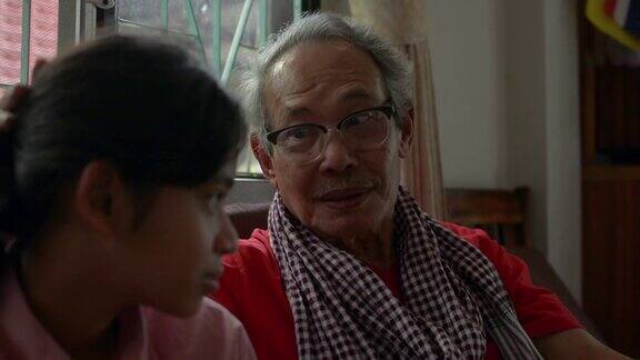 快乐的亚洲老爷爷戴着眼镜坐在客厅里和他可爱的十几岁的孙女聊天