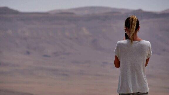 年轻女子用手机拍摄沙漠火山口全景照片