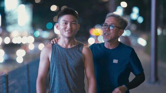亚洲华人活跃的老人和他的儿子在晚上一起跑步锻炼后散步聊天城市