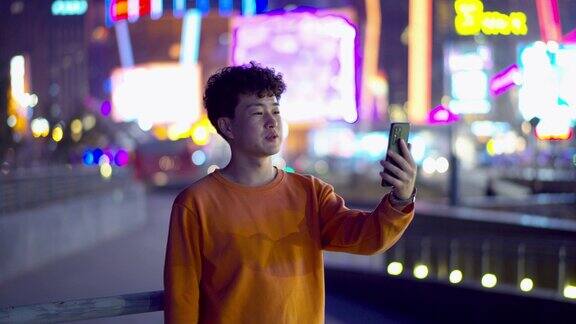 亚洲年轻帅哥晚上在城市街道上使用智能手机