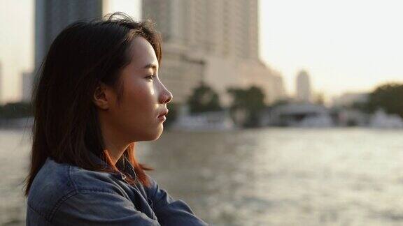 年轻的亚洲女性感到悲伤站在湄南河在泰国在美丽的日落