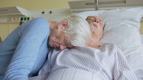在医院病床上一位老妇人在她生病的丈夫旁边哭泣