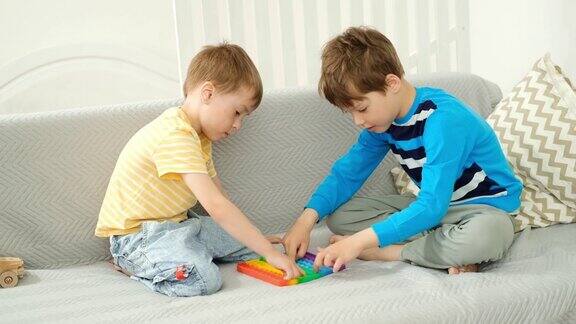 两个白人男孩坐在家里客厅的沙发上玩着抗压玩具