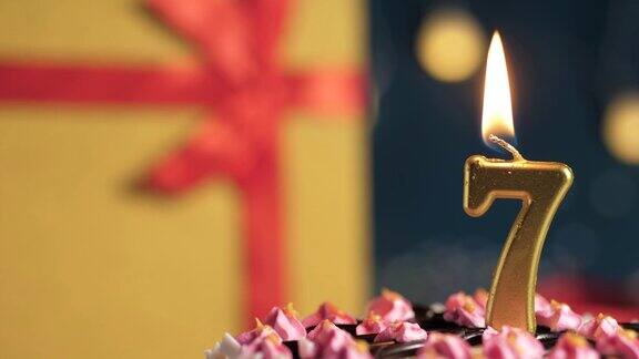 7号生日蛋糕用金色蜡烛点燃蓝色背景的礼物用红丝带绑在黄色盒子里特写和慢动作