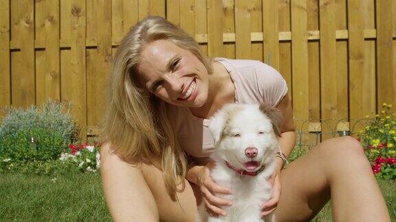 慢镜头:一个阳光明媚的日子快乐的金发女孩在后院抚摸她的狗